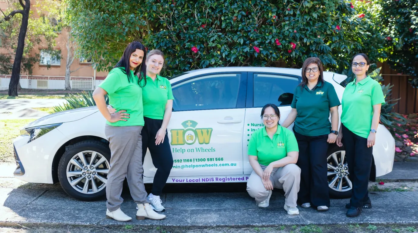 Help on Wheels team members in green uniforms beside their branded car