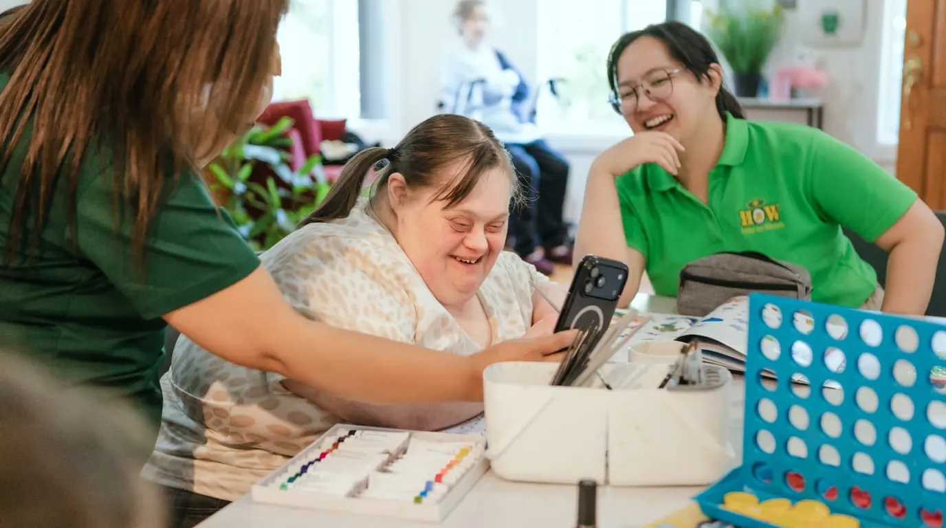 A Help on Wheels support worker laughing with a participant at an activity table