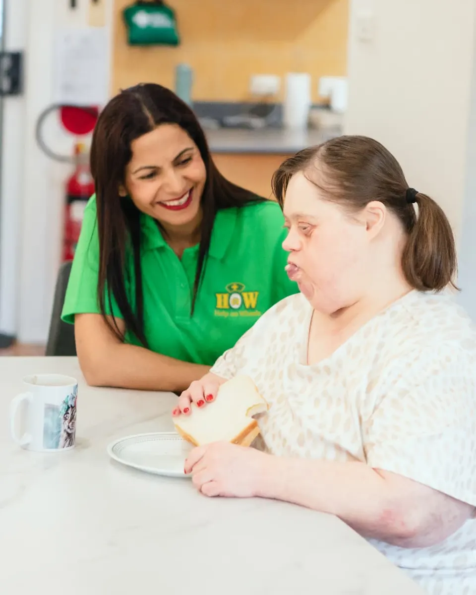 A Help on Wheels support worker sitting with a participant at the kitchen table during a meal