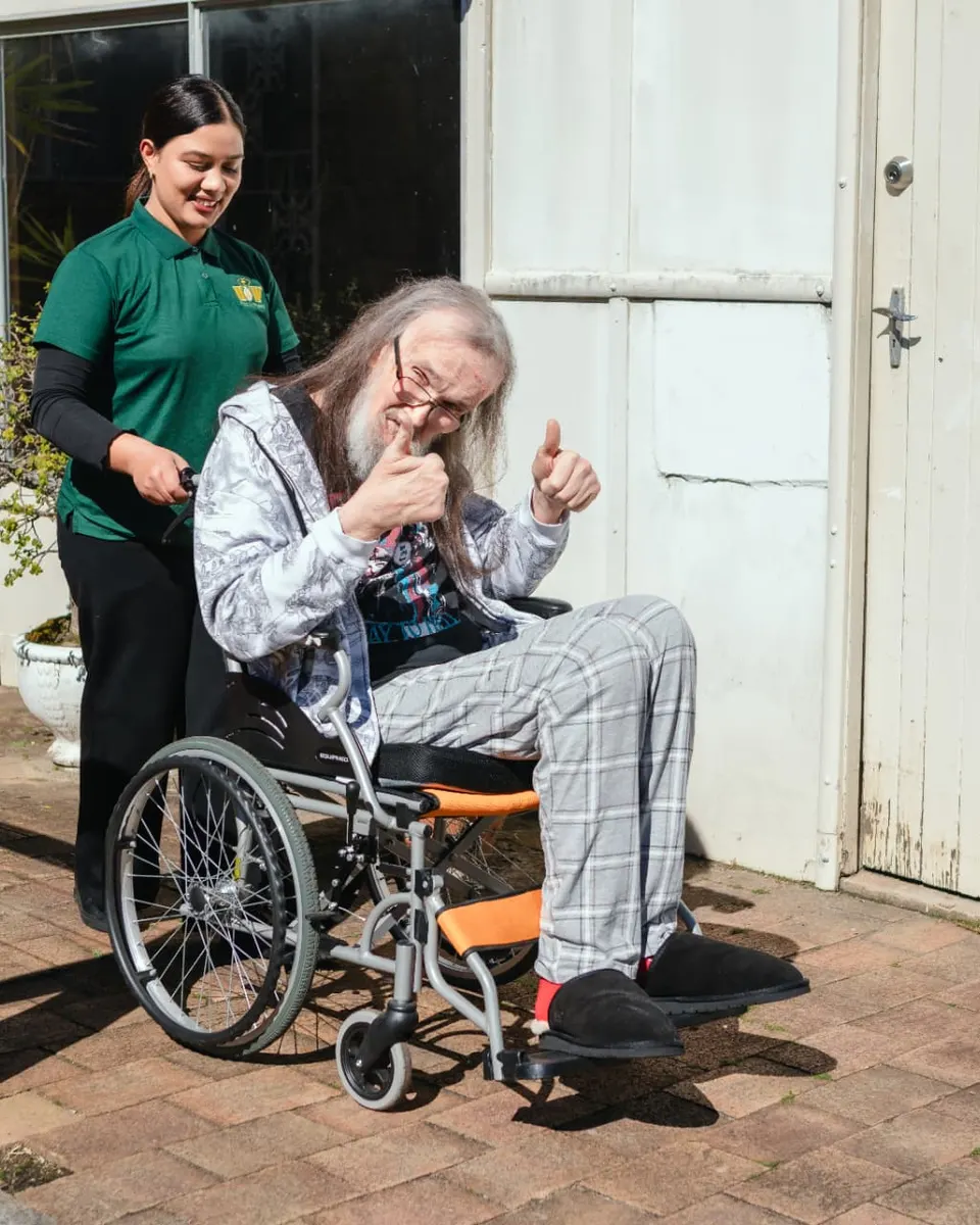 A Help on Wheels support worker outside with a participant in a wheelchair giving a thumbs up