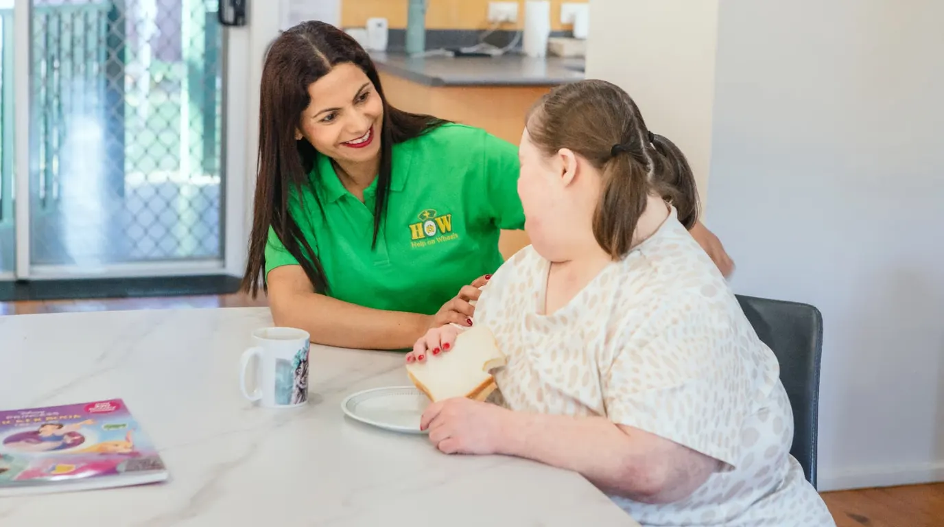 A Help on Wheels support worker sitting at a kitchen table with a participant, working through an everyday routine together