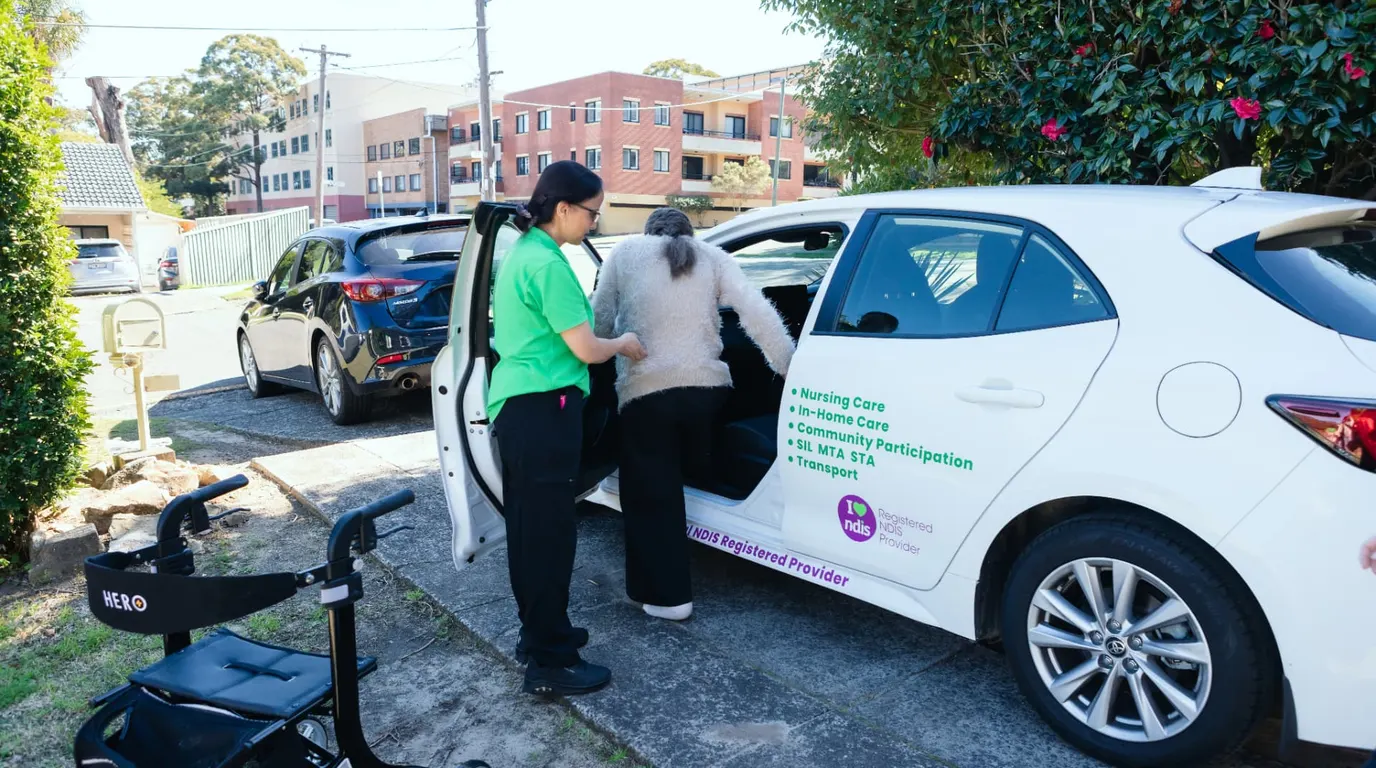 A Help on Wheels support worker helping a woman into the Help on Wheels car outside her home