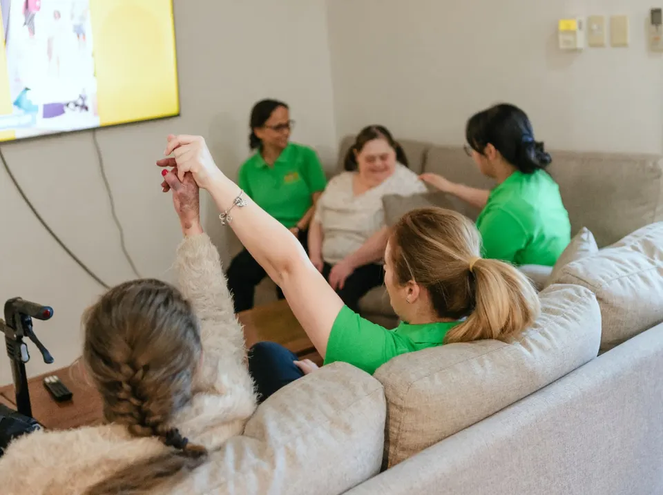 Participants and Help on Wheels support workers relaxing and laughing together in the living room