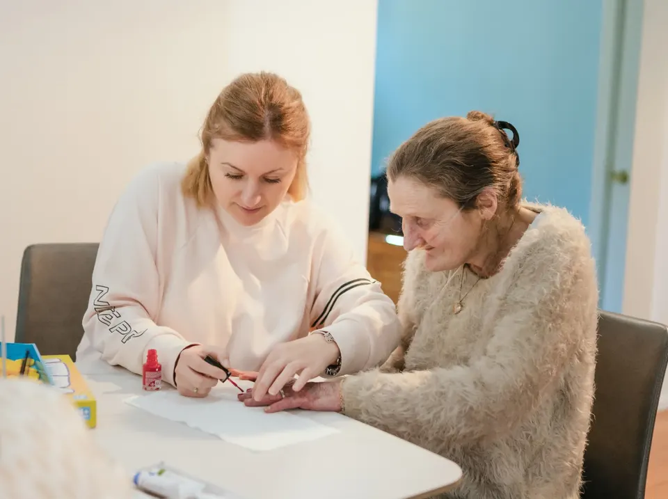 A Help on Wheels support worker painting a participant's nails together at the dining table