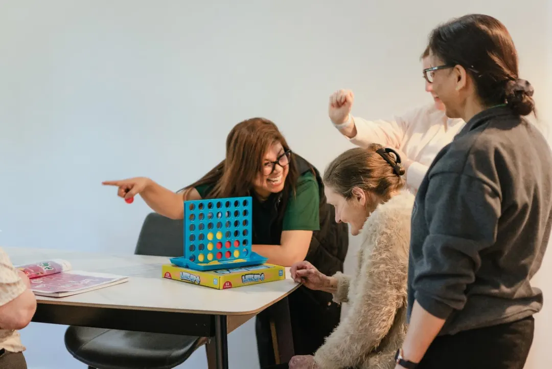 Support worker playing Connect Four with participants at a group activity