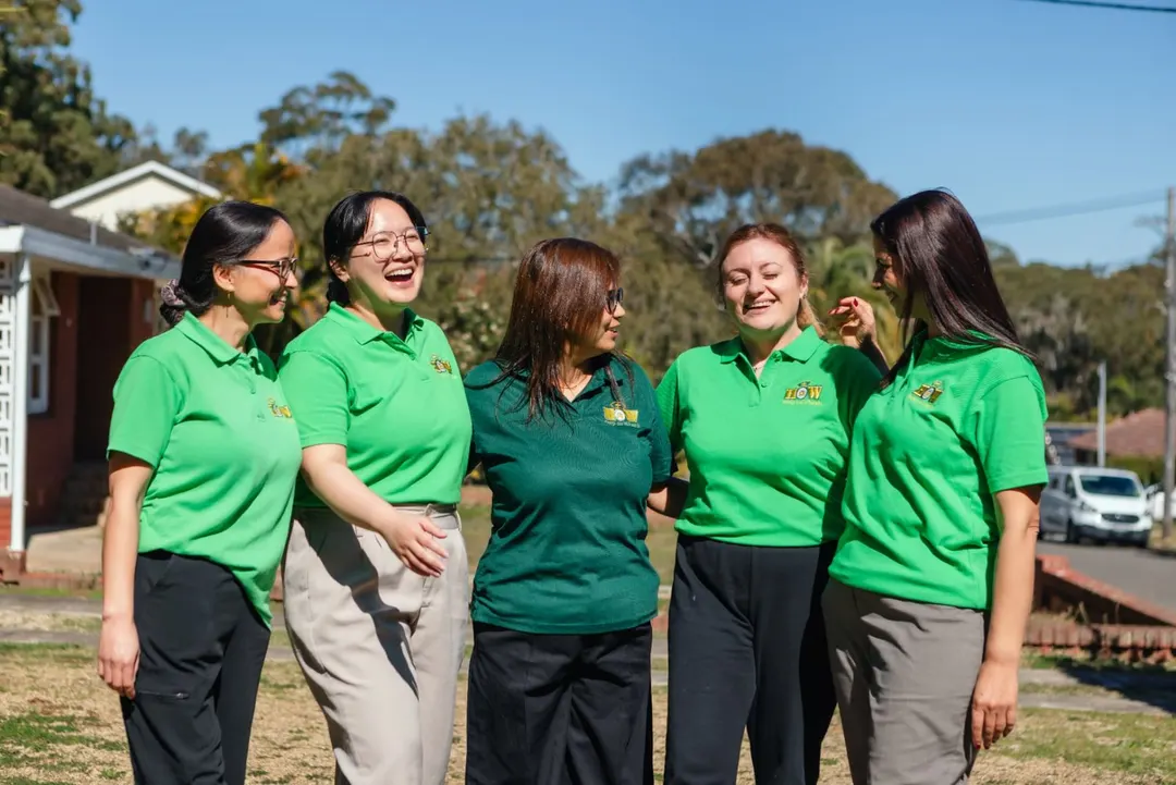 The Help on Wheels team smiling together outdoors in green uniforms