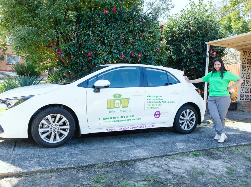 A Help on Wheels support worker standing beside the branded Help on Wheels car